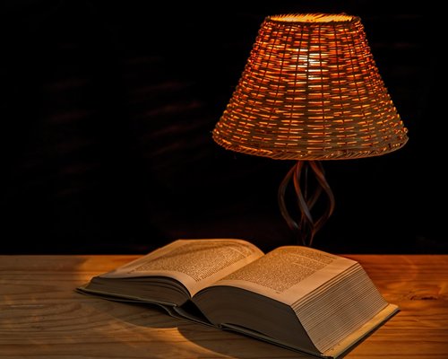 Person reading a book with warm lamp light in cozy Indonesian home at night